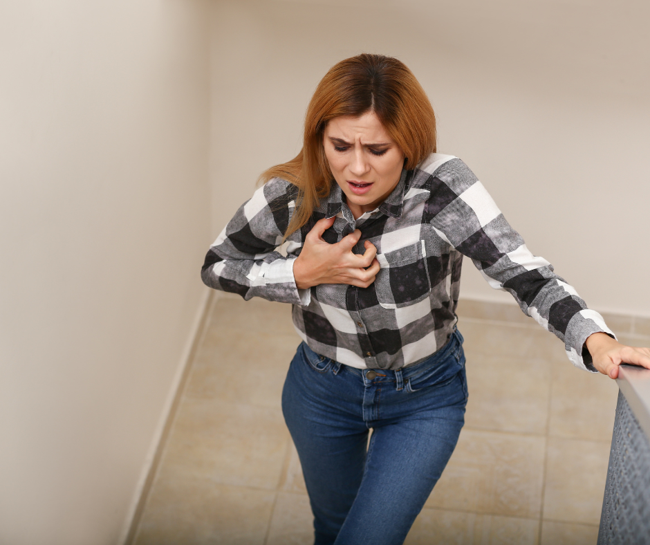 Woman in stairwell clutching chest, unsure if she is having an anxiety attack vs. panic attack.